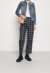 Denim jacket, white T-shirt, black and white plaid pants, black platform boots, and a small tan crossbody bag.