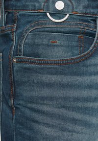 Jean en denim bleu foncé avec des coutures orange, présentant des poches avant et une fermeture à bouton en métal. Texture lisse et coupe classique.