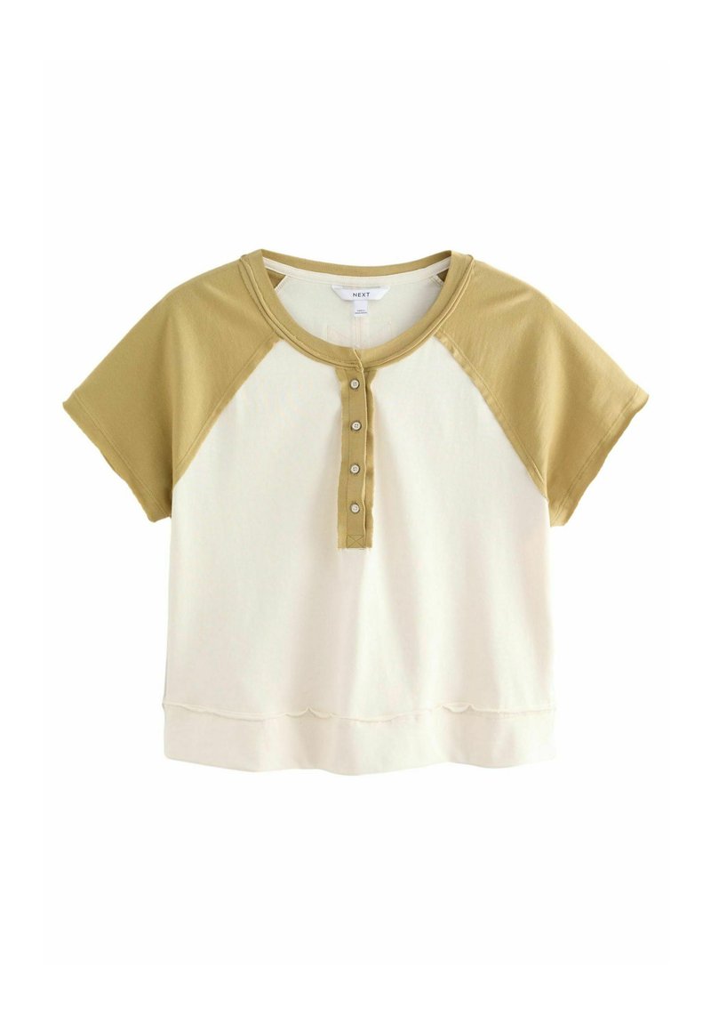 Camiseta de algodón con mangas raglán cortas, bicolor en crema y verde oliva, con una tapeta de botones y detalle de dobladillo ondulado.