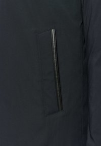 Czarna kurtka z gładkiego, eleganckiego materiału, z boczną kieszenią wykończoną cienkim, błyszczącym czarnym zamkiem. Czyste linie i minimalistyczny design.