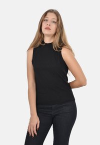 Top senza maniche di colore nero realizzato in tessuto a costine, con colletto alto e design aderente. Abbinato a jeans denim scuri.