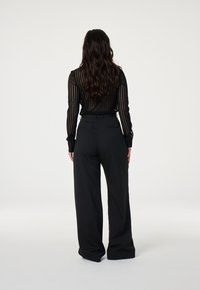 Black striped blouse with long sleeves and button cuffs paired with wide-leg black trousers, featuring a smooth texture and tailored fit.
