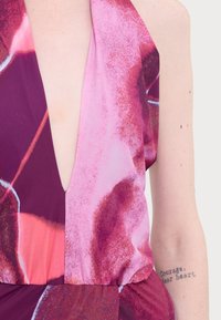 Abito con scollatura a V in una miscela di tonalità rosa e viola con motivi astratti. Tessuto morbido, vita cintrata e silhouette fluida.