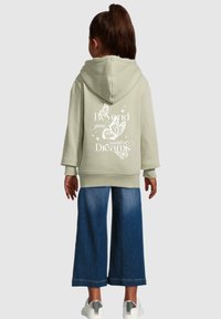 Olive green hoodie with a large butterfly graphic and text on the back, paired with wide-leg blue jeans and white sneakers.