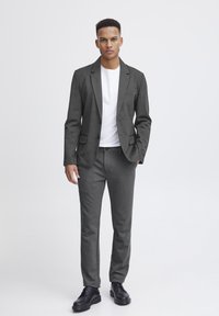 Grauer Blazer mit einem weißen T-Shirt darunter, kombiniert mit grauen Hosen und schwarzen Schuhen. Schlankes Design mit taillierter Passform und minimalen Hardware-Details.