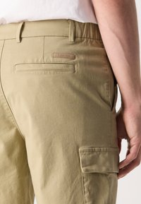 Khaki cargo pants with a smooth cotton blend, featuring side pockets and a subtle Calvin Klein label on the back pocket. Casual fit design.
