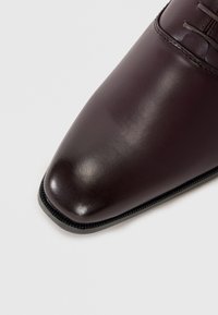 Chaussure habillée en cuir marron avec un bout pointu, une finition lisse et un bord arrondi. Elle présente des lacets et des détails de couture subtils le long de l'ouverture.