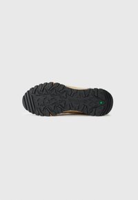 Black rugged rubber sole of a tan Timberland boot with deep treads and small green hexagonal logo near the heel.