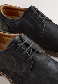 Chaussures habillées pour hommes en cuir noir à lacets, doublure intérieure fauve et coutures détaillées sur les côtés et la semelle.