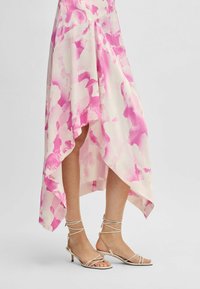 Rosa und weiß gemustertes Kleid mit asymmetrischem Saum, kombiniert mit leichten Sandalen mit Riemchen und niedrigem Absatz.