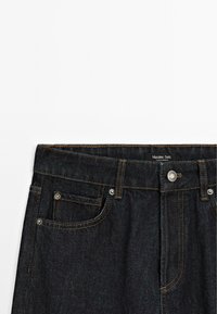 Donkerdenim jeans met een rechte snit, voorzien van een tailleband, twee voorzakken en contrasterende stiksels. Merktag zichtbaar op de tailleband.