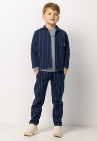 Marine gestreepte jas en broek set in zachte stof, met knopen, een borstzak en een lichtgrijs shirt eronder. Inclusief lichte sneakers.