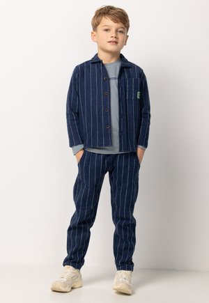 Marine gestreepte jas en broek set in zachte stof, met knopen, een borstzak en een lichtgrijs shirt eronder. Inclusief lichte sneakers.