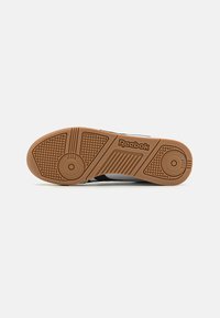 Semelle de sneaker Reebok présentant une semelle extérieure en caoutchouc gum texturé avec un motif circulaire, contrastée par un design supérieur noir et blanc.