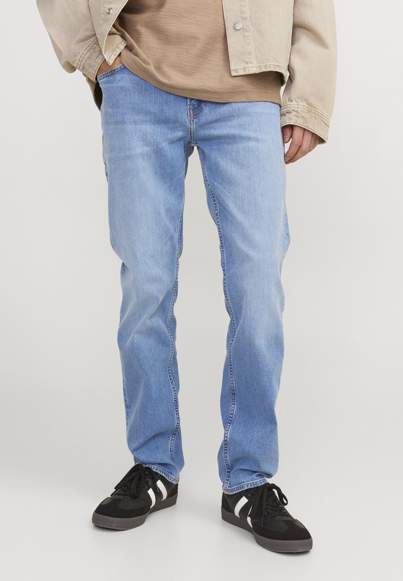 Světle modré džíny s rovného střihu, které mají klasický pětikapsový design a jemnou vybledlou texturu, nošené s černými teniskami.