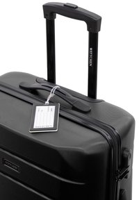 Harde zwarte koffer met een gestructureerd oppervlak, een uitschuifbare handgreep en een aangehechte bagagelabel. Heeft een ritssluiting en merklogo.