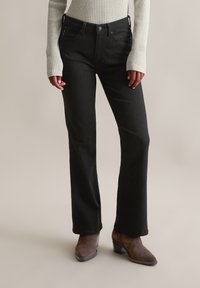 Jeans évasés noirs avec une taille ajustée, cinq poches et une texture lisse, assortis à des bottines à talons bruns.