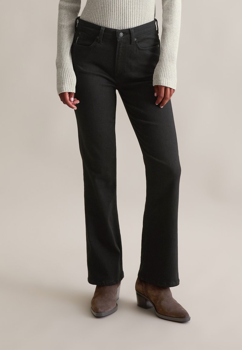 Jeans évasés noirs avec une taille ajustée, cinq poches et une texture lisse, assortis à des bottines à talons bruns.