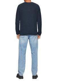 Granatowa, dzianinowa bluzka z długim rękawem i okrągłym dekoltem, zestawiona z jasnoniebieskimi dżinsami o prostym kroju. Czarne buty i widoczne detale haftu.