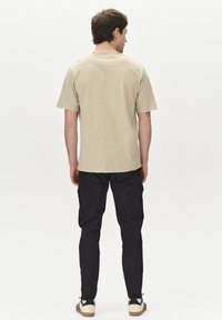Beige short-sleeve t-shirt with a relaxed fit, paired with black cargo pants featuring side pockets and a tapered leg. Casual footwear.