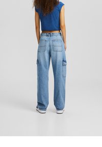 Light blue denim cargo pants with wide legs, multiple pockets, and a high waist, paired with a fitted dark blue cropped top.