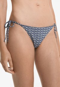 Tmavěmodré bikiny dolní části s vzorem s rybí kostí, s bočními šňůrkami. Vyrobené z elastického materiálu s hladkou texturou.
