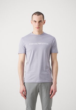 Camiseta de algodón lila claro con cuello redondo y mangas cortas, con un logo blanco de "Emporio Armani" en el pecho.