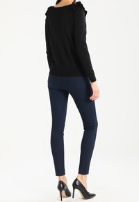 Zwarte trui met lange mouwen en gerimpelde accenten op de schouders, gecombineerd met donkerblauwe slim-fit jeans en zwarte hoge hakken.