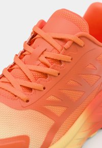 Sapatilha atlética laranja com malha texturizada e sobreposições sintéticas suaves. Apresenta atacadores combinando e uma sola amarela com degradê.