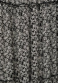 Svart tyg med ett vitt blommönster. Designen har små blommor och blad, med samlade veck och en volangkant.