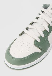 Biele a zelené kožené tenisky s perforovanou špičkou, plochými bielymi šnúrkami a hladkým textúrou; majú nízkoprsťový dizajn a kontrastné šitie.