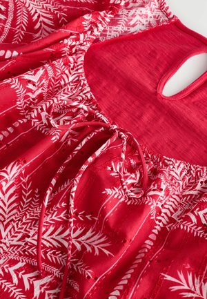 Tissu rouge avec un imprimé botanique blanc, encolure froncée avec liens, et une petite découpe dans le dos, mettant en valeur une texture légère.