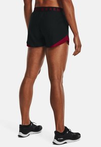 Černé sportovní šortky s vínovým pruhem po straně; elastický pas s logem "Under Armour". Nošeny s černými tréninkovými botami.