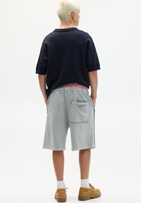 Dunkelblaues, übergroßes Poloshirt, hellgraue Jeansshorts mit Seitentaschen und beigefarbene Schuhe mit rutschfester Sohle. Minimalistisches Design mit weicher Textur.