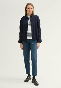 Marineblauwe lange mouw shirt over een wit en marineblauw gestreept shirt, gecombineerd met blauwe jeans en zwarte leren schoenen. Eenvoudig ontwerp, ontspannen pasvorm.