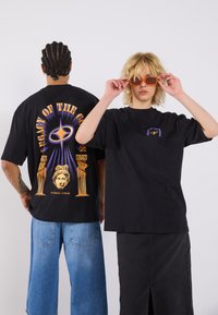Black graphic t-shirts feature bold text and imagery, with one displaying a design of columns and a statue. Accessories include orange sunglasses.