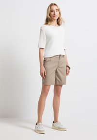 Béžové šortky vyrobené z lehkého materiálu, s bočními kapsami a zipovým zapínáním. V kombinaci s bílým strukturovaným pleteným topem a teniskami.