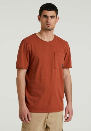 Rostfarbene kurzärmlige T-Shirt aus weichem Material, mit Rundhalsausschnitt und einer linken Brusttasche mit einem Markenlabel.