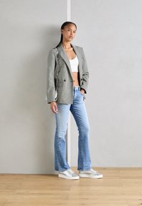 Dwurzędowa szara marynarka w jodełkę, biały krótki top, jasnoniebieskie dzwony i srebrne trampki. Minimalistyczne dodatki i naturalne włosy.