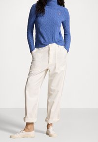 Vaaleansininen palmikkoneuleinen pooloneule, kermaan sävyiset leveälahkeiset housut edessä taskuilla ja kermaan sävytetyt kangastennarit käännetyin resorein.