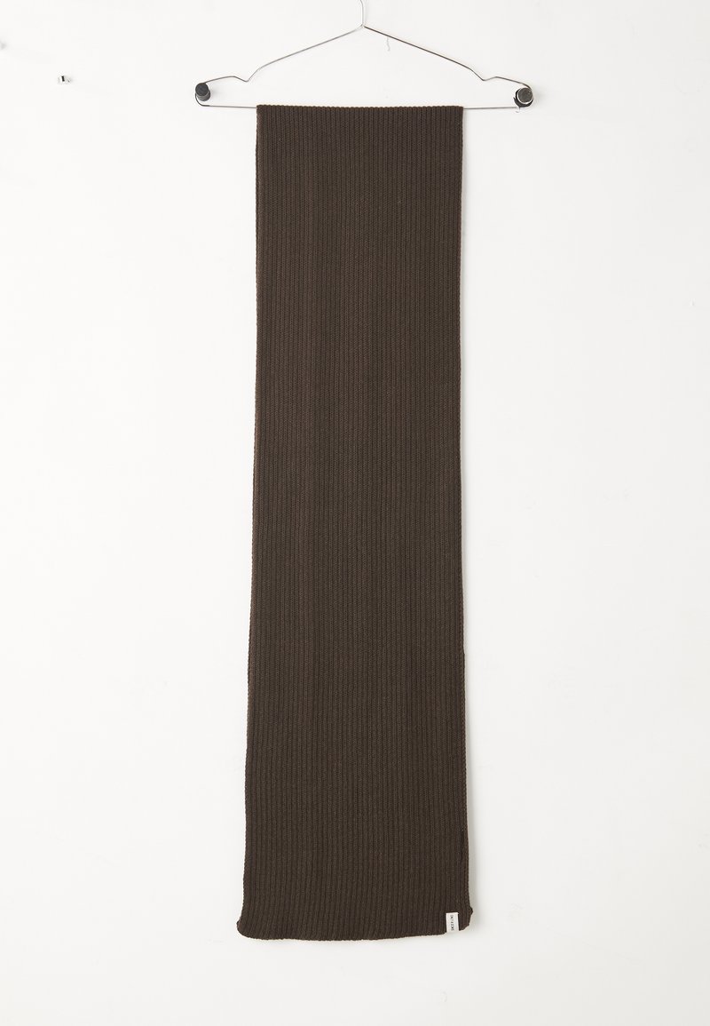 Écharpe en tricot côtelé marron foncé suspendue à un cintre en métal blanc sur un fond blanc uni.