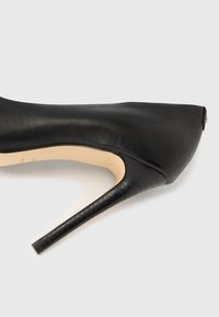 Svart høyhæl sko med en slank, spiss tå og teksturert lær overdel. Har en stilett-hæl og en glatt beige innside.