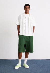 White embroidered short-sleeve shirt, white t-shirt, green shorts, and green patterned sneakers with white soles, styled with white socks.