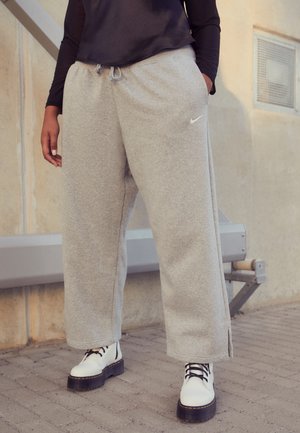 Personne portant un pantalon de survêtement gris à jambes larges avec le logo Nike, un haut à manches longues noir et des bottes blanches épaisses à lacets, debout en plein air.