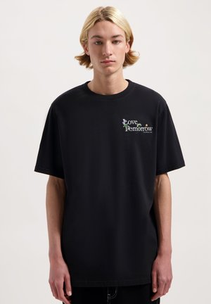 Zwarte katoenen t-shirt met korte mouwen, ronde hals, met "Love Tomorrow" borduurwerk in kleurrijke tekst op de linkerborst.