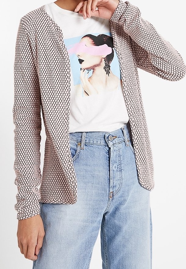 Personne portant un jean taille haute bleu clair, un t-shirt blanc avec illustration de femme et un cardigan beige à motifs ouvert sur le devant.