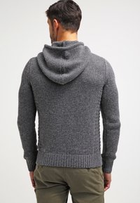 Szara, dziana bluza z kapturem z teksturowanym wzorem, prążkowanymi mankietami i dużym kapturem. Materiał wydaje się miękki i lekko puszysty.