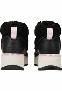 Zapatillas negras con parte superior de textil esponjoso, lengüeta trasera rosa y logotipo "TOMMY JEANS" en relieve. Presentan una gruesa suela de goma crema y detalles texturizados.
