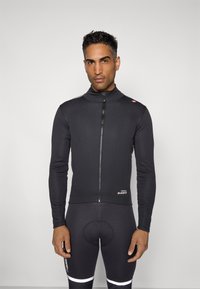 Schwarze Radfahrjacke mit Reißverschluss vorne und hohem Kragen, ausgestattet mit langen Ärmeln und einem eleganten Design. Getragen mit passenden schwarzen Radsportshorts.