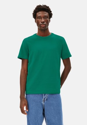 Grünes Baumwoll-T-Shirt mit Rundhalsausschnitt, kurzen Ärmeln und lockerer Passform. Der Stoff hat eine glatte Textur und wird mit hellblauen Jeans kombiniert.